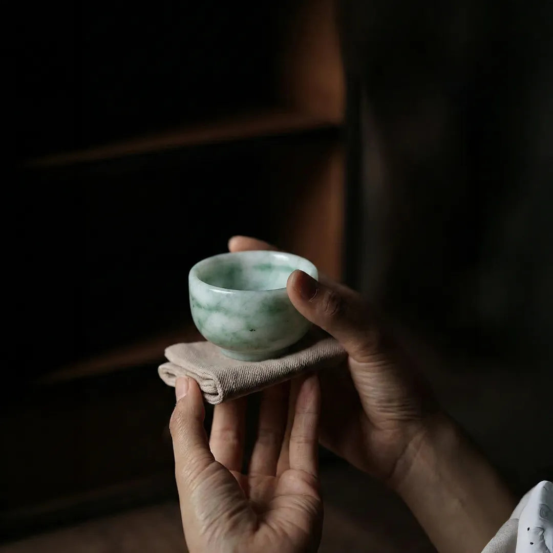 Person holding a small green ceramic cup with a cloth in a dimly lit setting