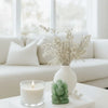Decorative setup with a candle, green statue, and vase with dried flowers on a table.