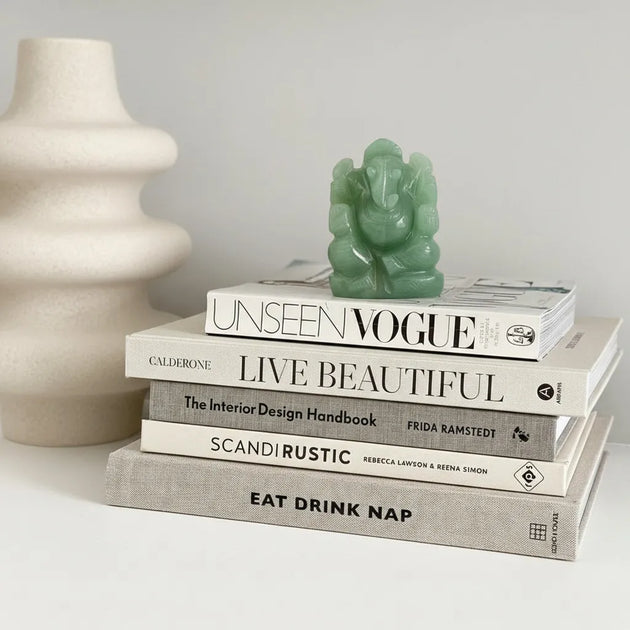Stack of books with a green statue on top, next to a beige vase.
