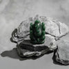 Green stone statue of a seated figure on gray stones with a neutral background