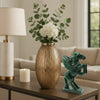 Decorative items on a table including a vase with flowers, a lamp, a candle, and a green figurine.