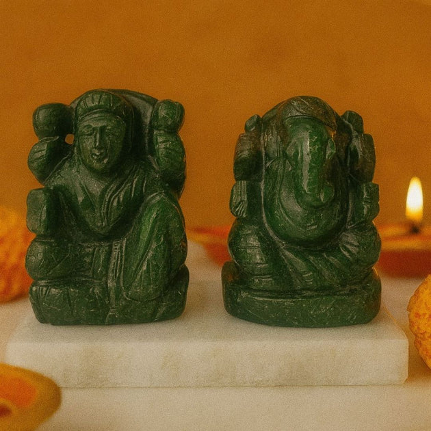 Two green stone statues of lakshmi ganesh on a white platform with an orange background