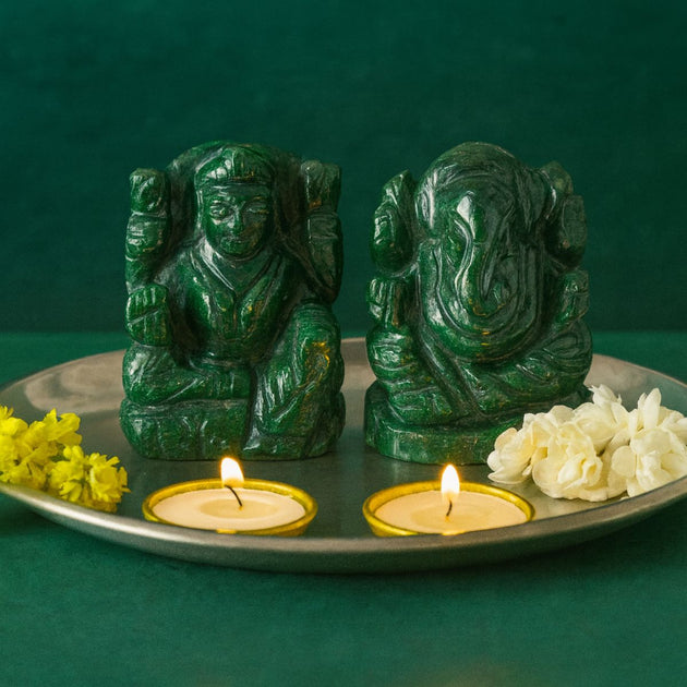 Two green aventurine stone Lakshmi Ganesh pair on a tray with two lit candles and flowers on a dark green background