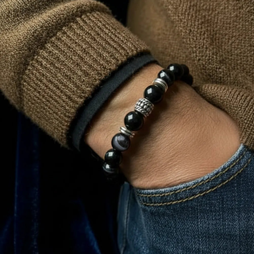 Close-up of a person wearing a black beaded bracelet with a brown sweater and blue jeans.