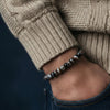 Close-up of a person wearing a beaded bracelet with a beige sweater and dark jeans.