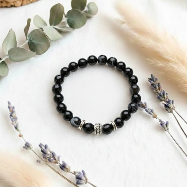 Black beaded bracelet with silver charm on a white surface with decorative elements
