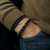 Person wearing a silver beaded bracelet on a dark background