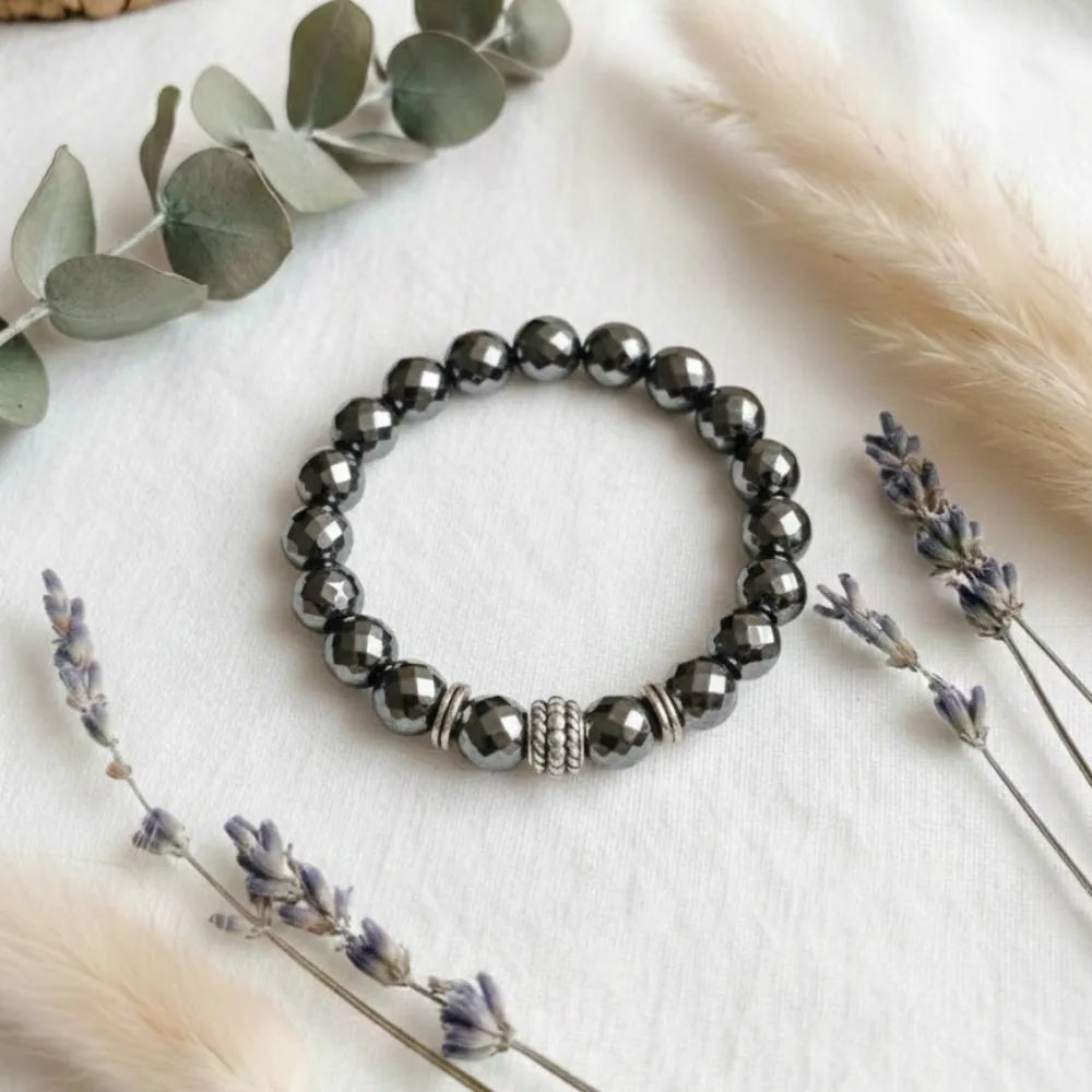 Bracelet with dark beads on a white surface with eucalyptus and lavender.