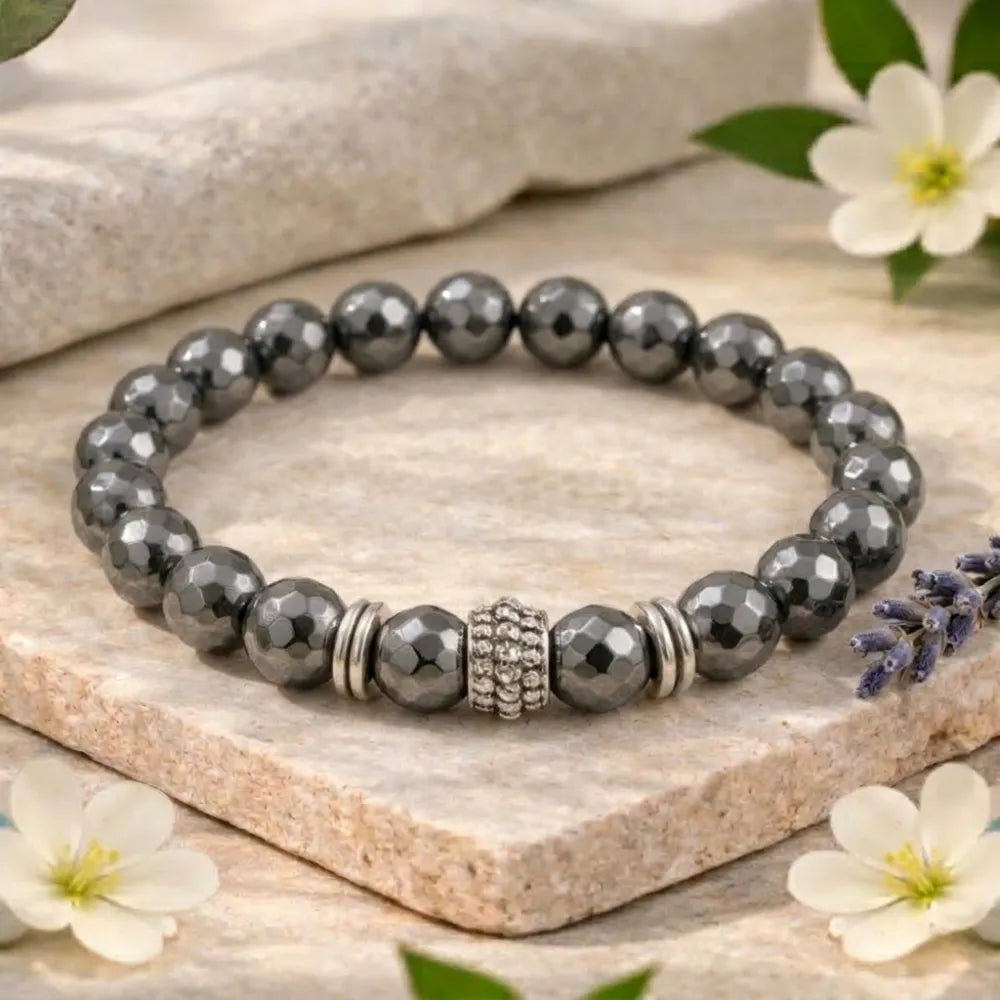 Gray beaded bracelet with silver accents on a stone surface with flowers