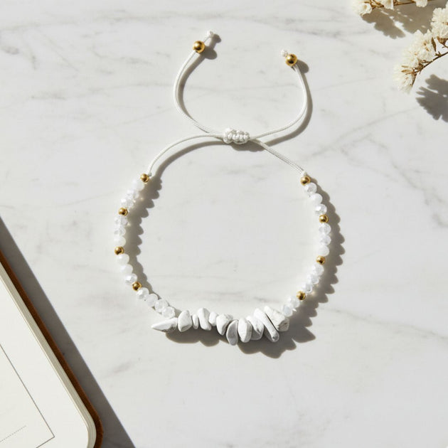 White beaded thread bracelet with gold accents on a light marble surface