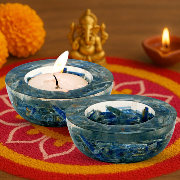Two blue orgonite candle holders with lit candles on a colorful mat with decorative elements.