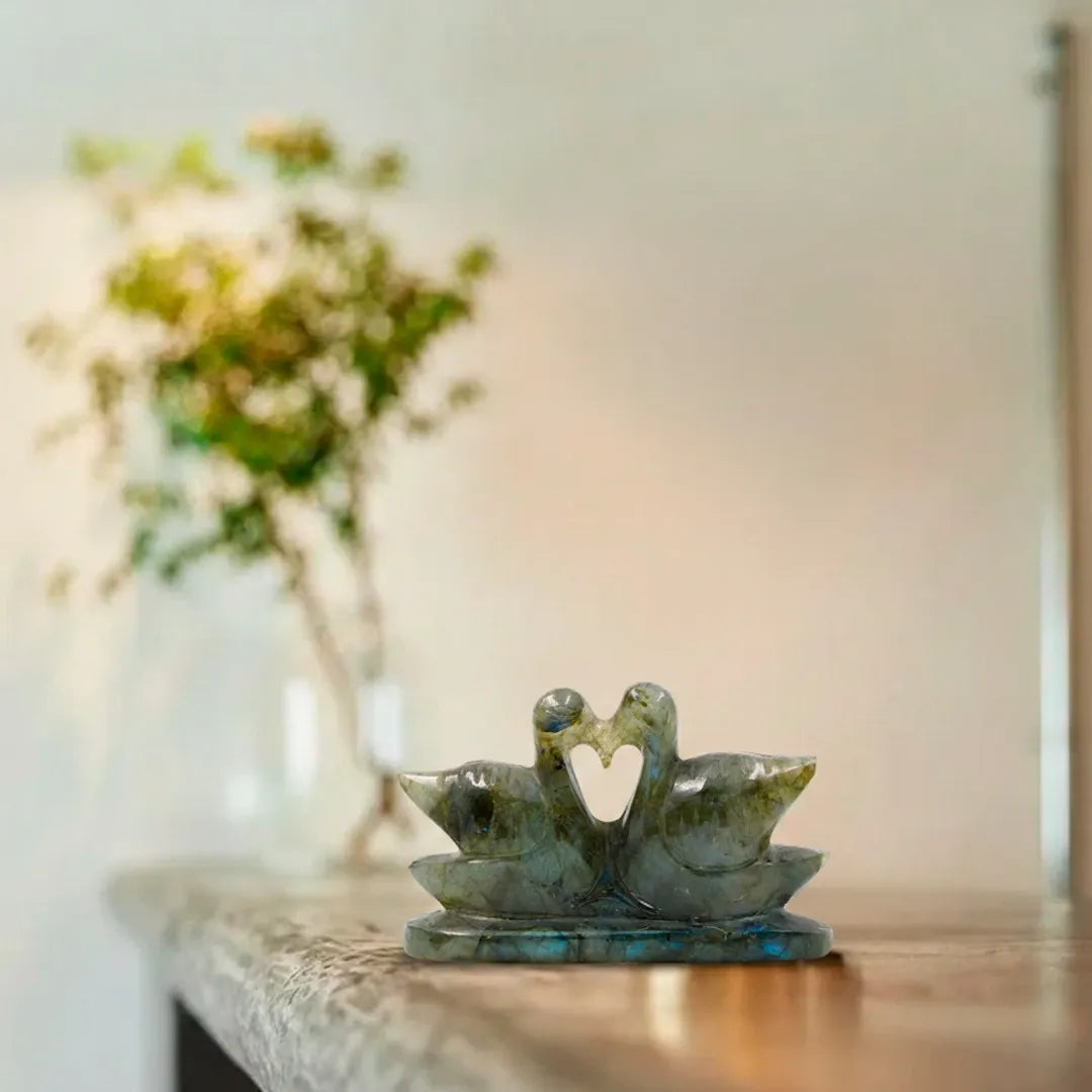Decorative sculpture of two swans on a table with a blurred floral background