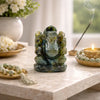 Green stone Ganesh statue on a marble surface with incense and flowers.