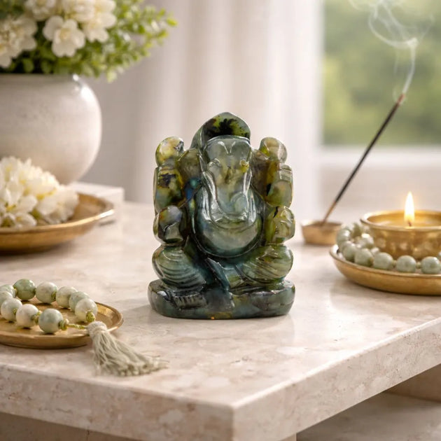 Green stone Ganesh statue on a marble surface with incense and flowers.