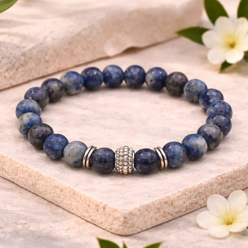 Blue beaded bracelet with a silver clasp on a wooden surface with flowers.