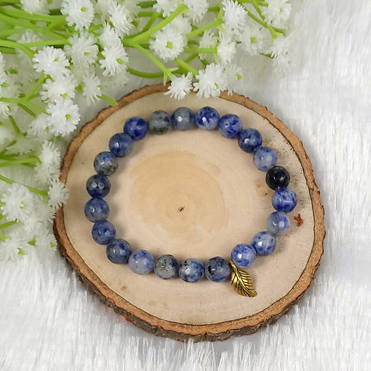 Blue beaded lapis lazuli bracelet with a gold accent on a wooden slice with white flowers in the background