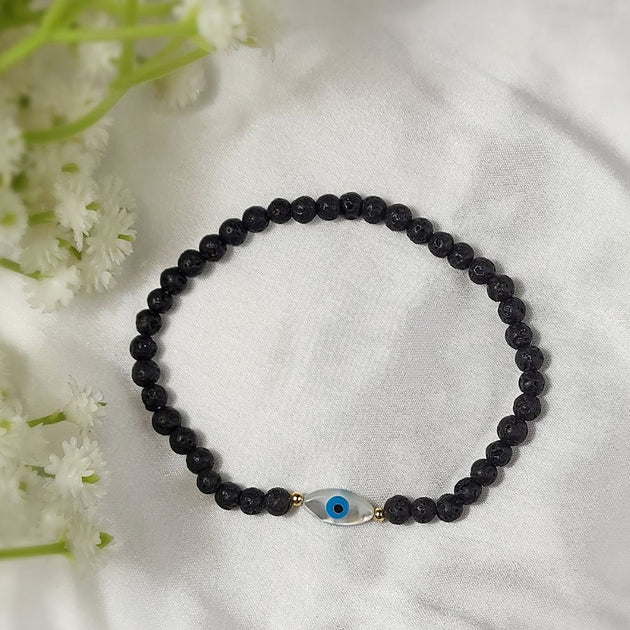 Black beaded bracelet with a blue evil eye charm on a white fabric background with white flowers.