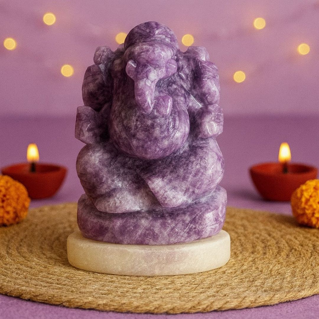 Purple stone statue of Ganesha on a woven mat with candles and marigold flowers in the background.
