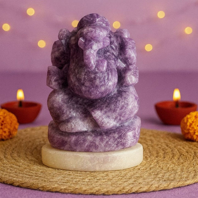 Purple stone statue of Ganesha on a woven mat with candles and marigold flowers in the background.