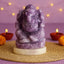 Purple stone statue of Ganesha on a woven mat with candles and marigold flowers in the background.