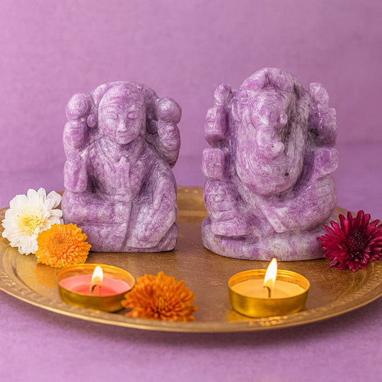 Two purple stone Lakshmi Ganesha pair on a golden tray with candles and flowers against a purple background