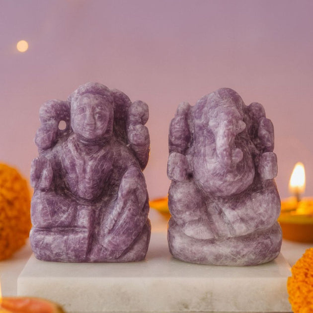 Two purple stone statues of lakshmi ganesha on a white surface with a blurred background