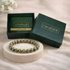 Gold beaded bracelet on a white stand with 'CALMINDS' branded box in the background