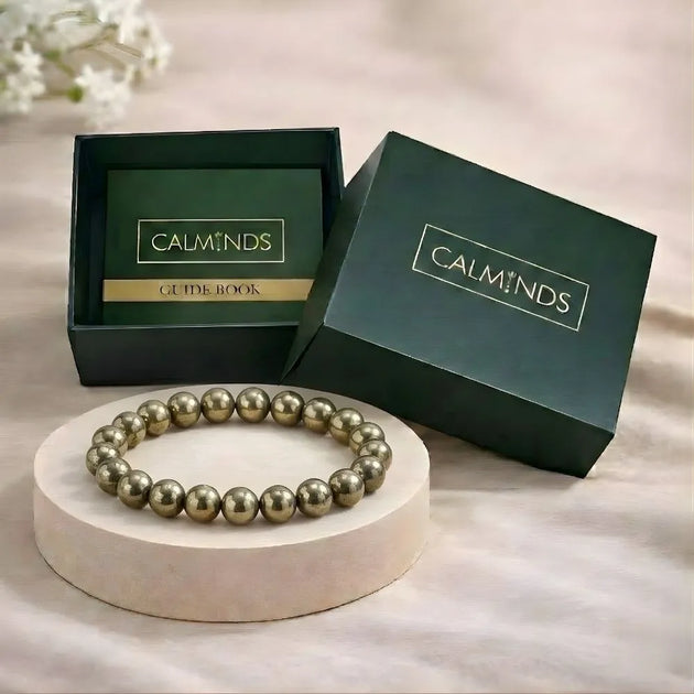 Gold beaded bracelet on a white stand with 'CALMINDS' branded box in the background