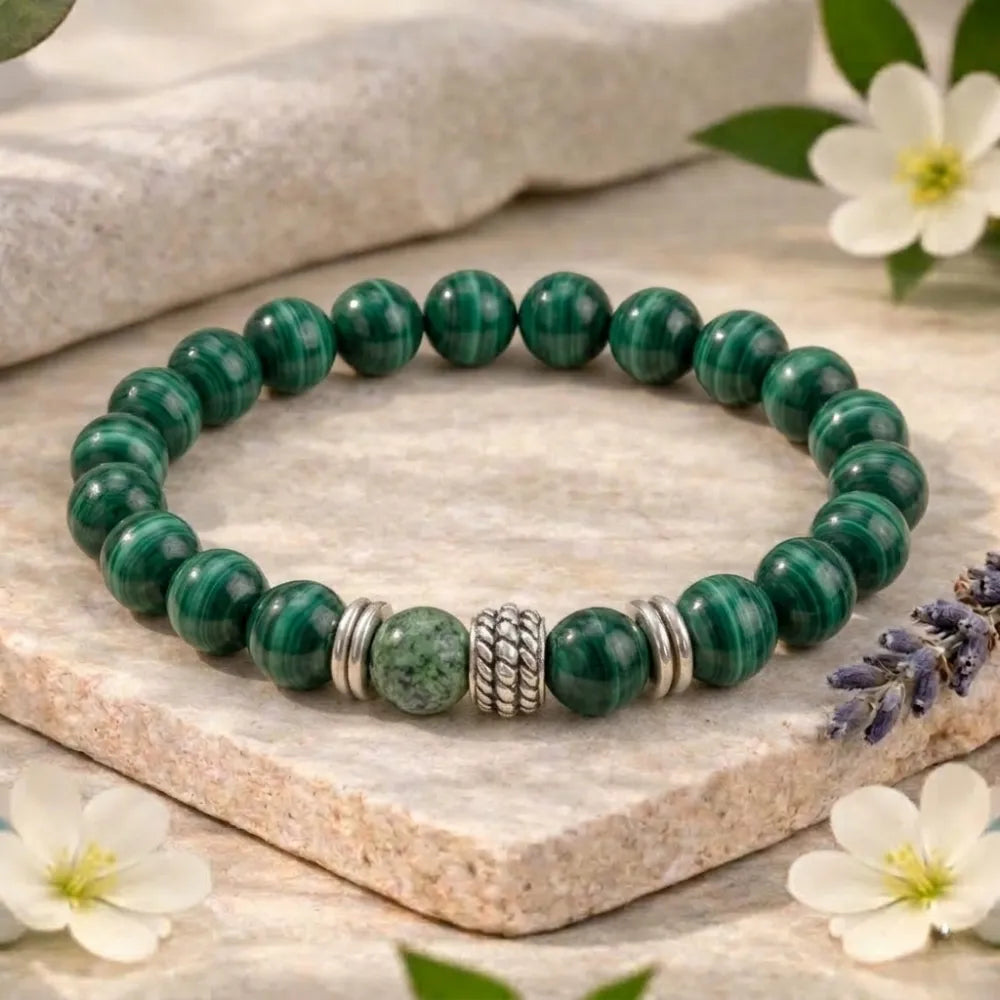 Green beaded bracelet with silver accents on a stone surface with flowers