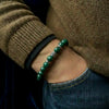 Green beaded bracelet on a wrist with a brown sweater and blue jeans.