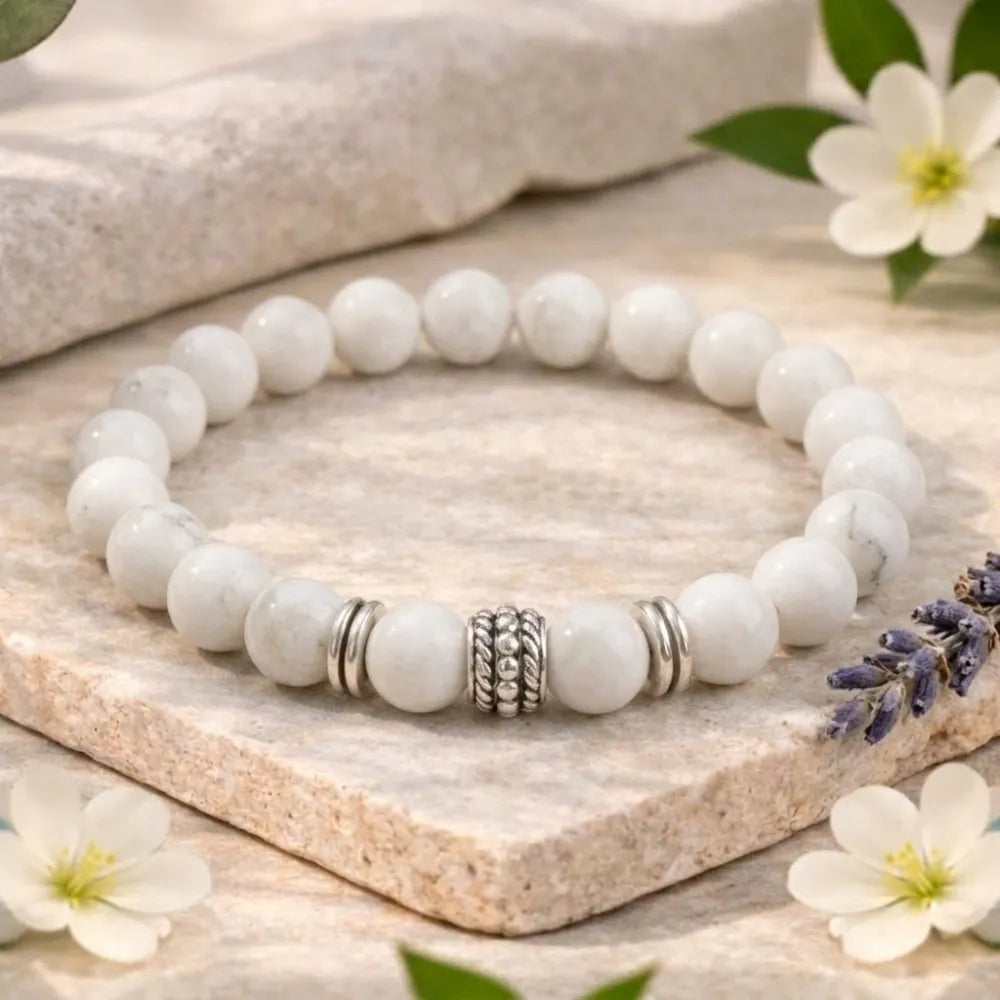 White beaded bracelet with silver charms on a stone surface with flowers
