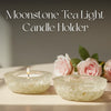 Two moonstone tea light candle holders with a lit candle and pink roses on a neutral background.