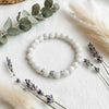 White beaded bracelet with silver accents on a white surface with lavender and eucalyptus leaves.