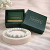 White beaded bracelet on a round wooden platform with 'CALMINDS' branded box in the background.