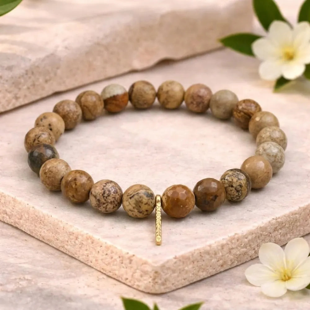 Beaded bracelet with a gold charm on a light stone surface with flowers.