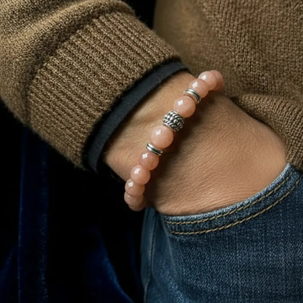 Close-up of a hand wearing a pink beaded bracelet with silver accents, against a dark background.
