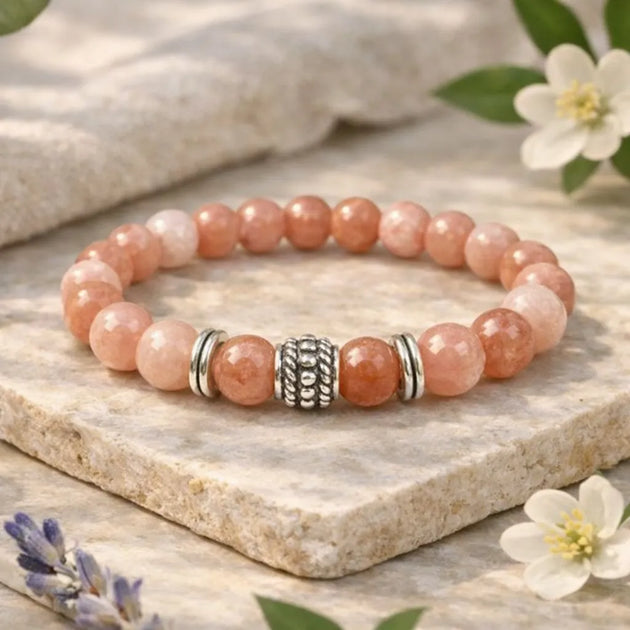 Pink beaded bracelet with silver accents on a stone surface with flowers and leaves.