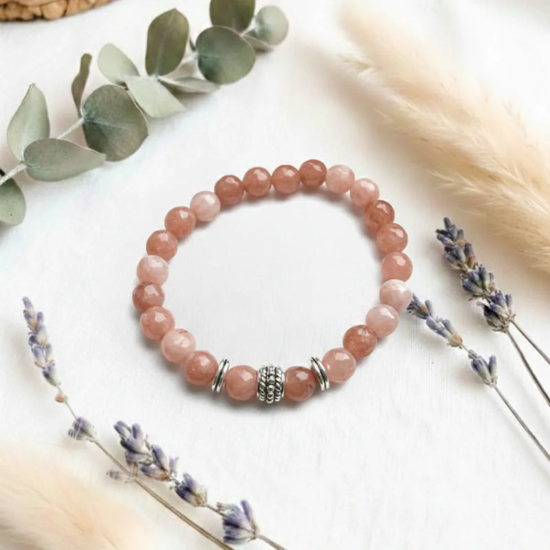 Pink beaded bracelet on a white surface with dried lavender and eucalyptus leaves.