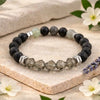 Black and gray beaded bracelet on a stone surface with flowers