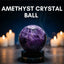 Amethyst crystal ball with candles in the background on a dark surface