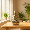 Gold Buddha statue on a wooden table with plants in the background