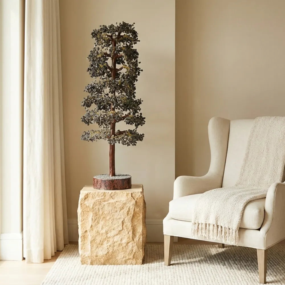 Decorative tree on a stone pedestal next to a beige armchair in a room with neutral walls and curtains.