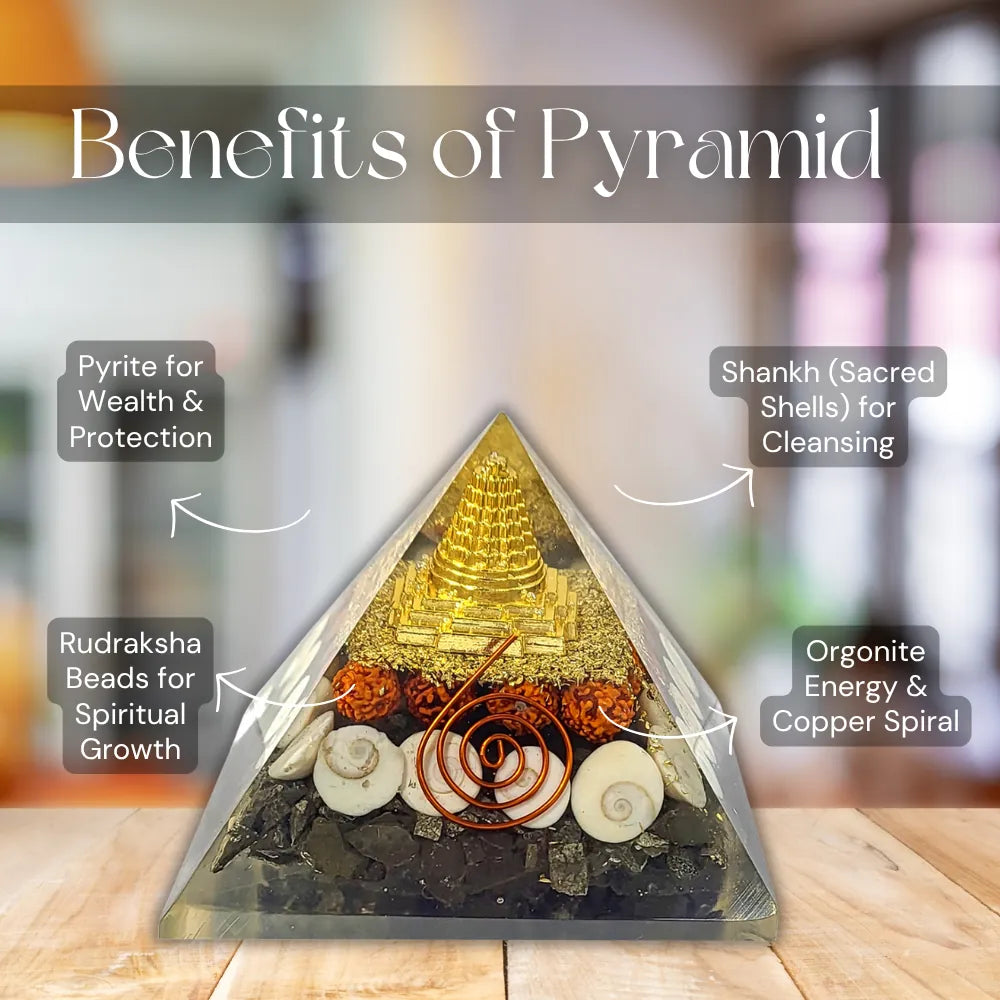 A clear acrylic pyramid crystal tower with a gold-toned central structure, copper spiral, white and beige shells, and dark stones, shown on a wooden surface with overlaid text reading 'Benefits of Pyramid' and callouts for pyrite, Shankh shells, rudraksha beads, and organite energy and copper spiral.
