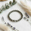Bracelet with gray beads on a white surface with lavender and eucalyptus leaves.