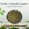 Pyrite crystal coaster with geometric design on a wooden base, surrounded by greenery.