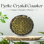 Pyrite crystal coaster with geometric design on a wooden base, surrounded by greenery.