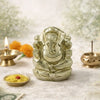 Decorative Ganesh statue with incense, flowers, and a lighted lamp on a textured surface.