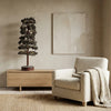 Beige armchair with a blanket next to a wooden side table with a plant, against a beige wall.