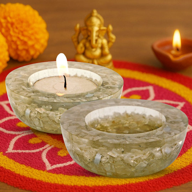 Two stone candle holders with lit candles on a colorful fabric background.