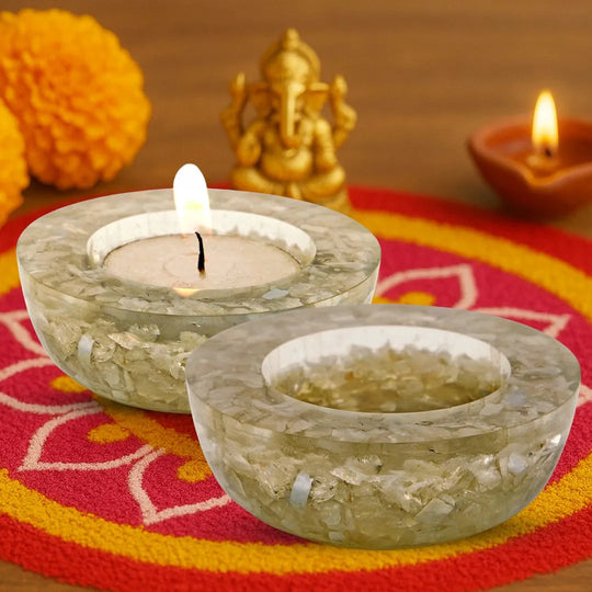 Two stone candle holders with lit candles on a colorful fabric background.